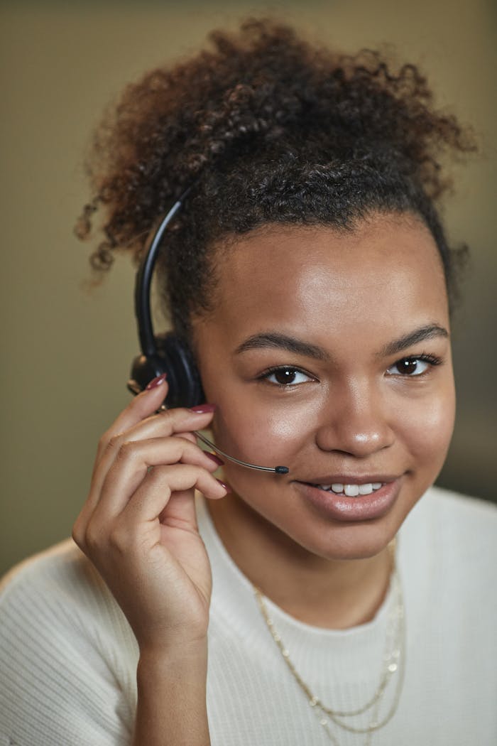 Close-up of a smiling woman with afro hair wearing a headset, providing customer support.